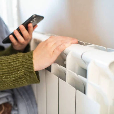 chauffage_electrique-_1_ personne qui touche le radiateur électrique avec son téléphone en main